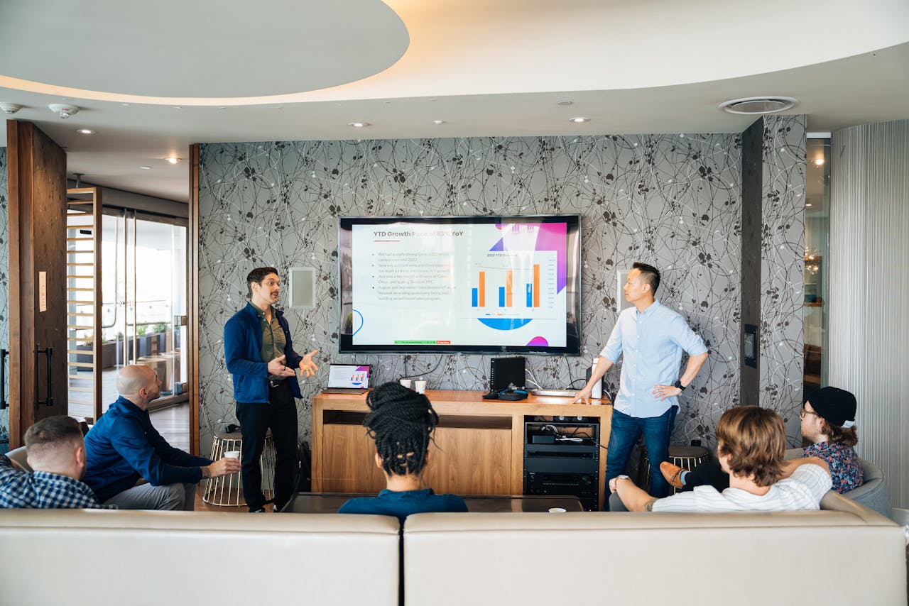 Group of professionals engaging in a business presentation with a TV displaying graphs.
